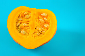 Half of an orange pumpkin with seeds on a turquoise background
