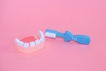 A wooden model of a jaw and tools for daily dental care, examination and prevention of caries on a pink background. Dental concept banner with copy space. Children's toy doctor

