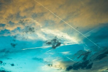 Beautiful poetic photo of a sky with clouds at sunset dusk with nice pastel yellow blue and pink colors, with airplane contrails  - Powered by Adobe