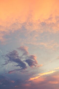 Beautiful poetic sot of a sky with clouds at sunset dusk with nice pastel yellow blue and pink colors, with airplane contrail 