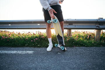 Young athletic man stand on side of road, hold longboard or skateboard. Ready to skate any moment. Moody summer cinematic image of youth and freedom