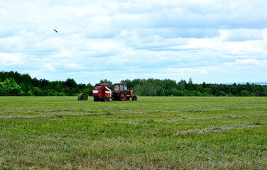 tractor on the green field making rolled haystacks with cloudy sky on background 