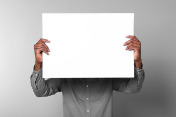 African American man holding sheet of paper on grey background. Mockup for design