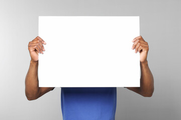 African American man holding sheet of paper on grey background. Mockup for design