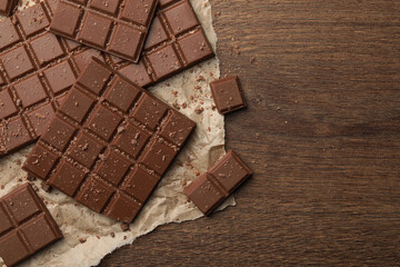 Pieces and crumbs of tasty chocolate bars on wooden table, top view. Space for text