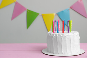 Delicious cake with cream and candles on pink wooden table. Space for text