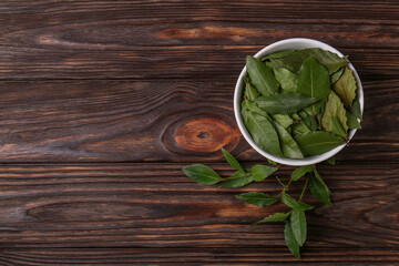 Fresh green bay leaves in bowl on wooden table, flat lay. Space for text
