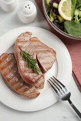 Delicious tuna steaks with rosemary and salad served on white marble table, flat lay