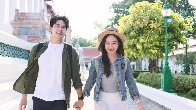 Asian attractive romantic couple travel in Bangkok city for honeymoon trip. Young new married man and woman backpacker tourist holding hands while walking in the temple and enjoying time together