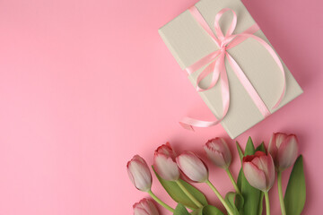 Beautiful gift box with bow and tulips on pink background, flat lay. Space for text
