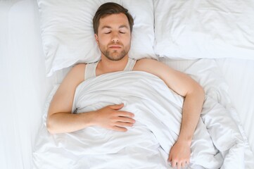 Handsome man sleeping under soft blanket in bed at home