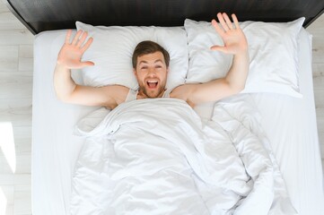Fototapeta na wymiar Cheerful Man Waking Up Lying In Cozy Bed At Home On Weekend Morning. Healthy Sleep Concept