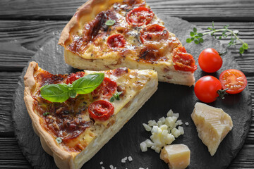 Pieces of delicious homemade quiche with prosciutto and ingredients on black wooden table, closeup