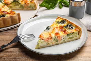 Piece of delicious homemade salmon quiche with broccoli and fork on wooden table