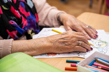 Elderly woman painting color on her drawing. Hobby at nursing home. High quality photo