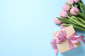 Beautiful gift box and bouquet of pink tulip flowers on light blue background, flat lay. Space for text