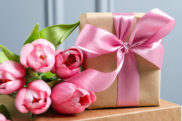 Beautiful gift box with bow and pink tulip flowers on grey background, closeup