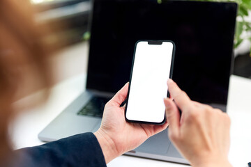 A brunette woman holding a mobile phone typing on a blank white screen.