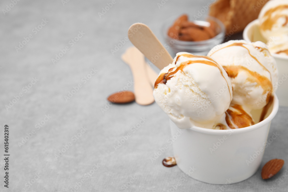 Wall mural scoops of ice cream with caramel sauce in paper cup on light grey table, closeup. space for text