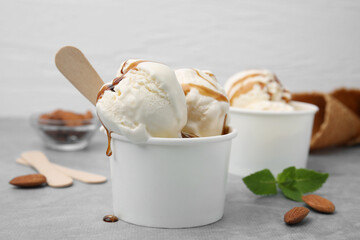 Scoops of ice cream with caramel sauce in paper cup on light grey table, closeup