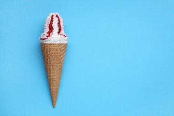 Delicious ice cream with raspberry jam in waffle cone on light blue background, top view. Space for text
