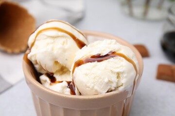 Scoops of ice cream with caramel sauce and candies on light grey table, closeup