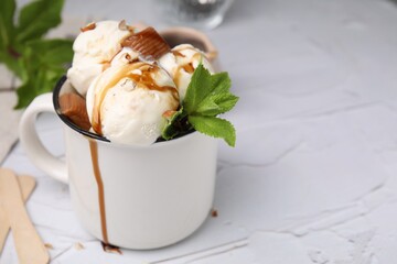 Scoops of ice cream with caramel sauce, candies and mint leaves on white textured table, closeup. Space for text