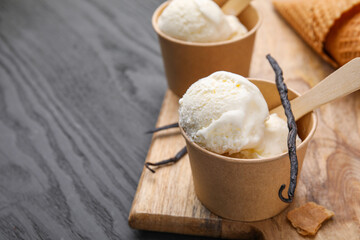 Paper cups with delicious ice cream and vanilla pods on grey wooden table, closeup. Space for text