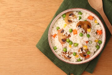 Bowl of delicious rice with vegetables on wooden table, top view. Space for text