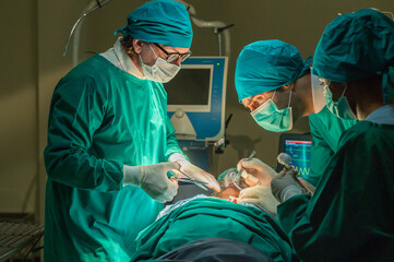 Team of surgery doctor in Operating Room, Assistant Hands out Instruments to Surgeons During Operation. doctor and nurse surgeons in green gown coat at hospital operating theater.