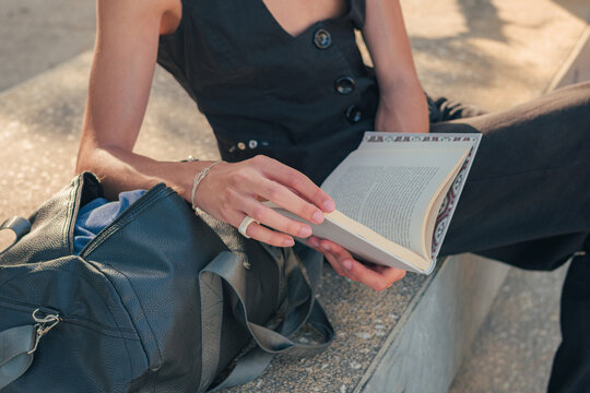 Close-up of a young fashionable man in black clothes reading a book in a park