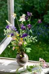 Bouquet of wild flowers in a vase on a wooden window sill. Floral decoration on the window of an old country house, summer cottage. Country life aesthetics