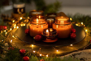 Soy candles burn in glass jars. Comfort at home. Candle in a brown jar. Scent and light. Scented handmade candle. Aroma therapy. Christmas tree and winter mood. Cozy decor. Festive garland decoration