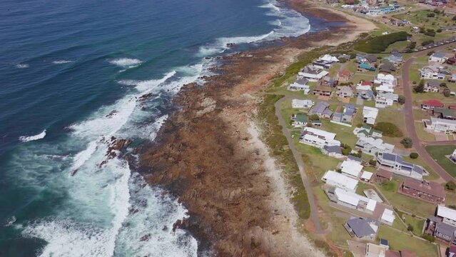 Still Bay aerial drone cinematic beach small surf town Garden Route South Africa Jeffreys Bay homes and buildings waves crashing on reef late morning afternoon forward pan up movement