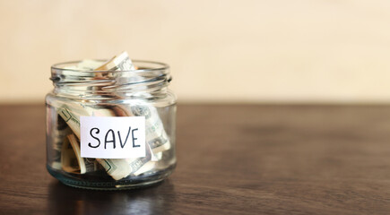 Save money for the future. Save. Glass jar with dollars on a wooden table. Piggy bank with banknotes, copy space. The concept of financial savings