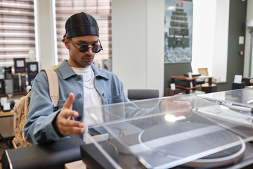 Portrait of young black man carefully opening record player in music store, copy space