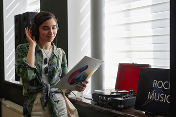Waist up portrait of smiling young woman listening to vinyl records in music store, copy space