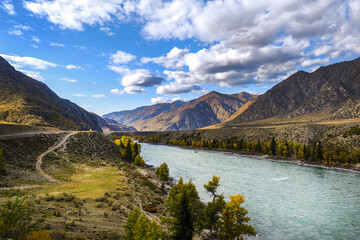Serpentine river among the mountain peaks. Mountain lake reflects the autumn landscape of the forest with yellow leaves. Stones in a mountain river. 