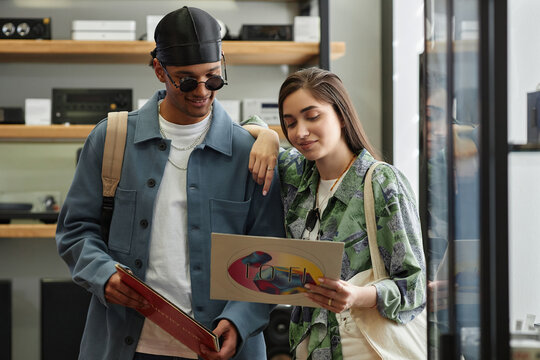 Waist up portrait of smiling young couple choosing vinyl records in music store