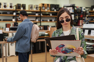 Waist up portrait of young woman holding set of vinyl records in music store, copy space