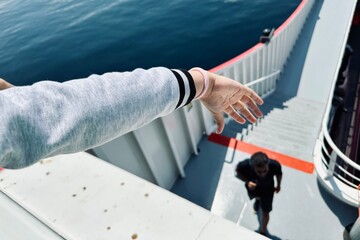 Scene from a ferryboat to greek islands where a child hand is extended over the railing and a silhouette beneath. - 615417194
