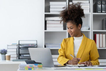 African American businesswoman working on laptop at desk, sitting, thinking, analyzing, recording data, planning in financial business from documents in modern office, happily.