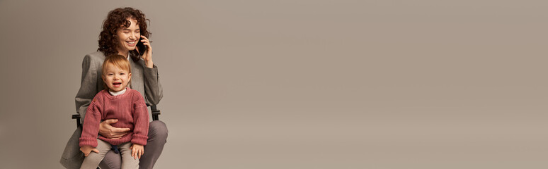 balanced lifestyle, phone call, happy businesswoman talking on smartphone and sitting on chair with child on grey background, motherhood, multitasking, work life balance concept, banner