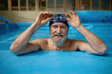 Portrait of mature senior man wearing swimming hat and goggles at pool