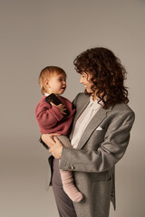 modern parenting, building successful career, balancing between work and life, cheerful mother holding in arms toddler daughter with smartphone on grey background, career and family