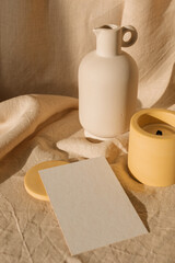 Empty card, ceramic vase, candle on linen fabric. Showcase  of designs in an aesthetic setting.