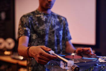 Closeup of young black man playing vinyl records at record player at home, copy space