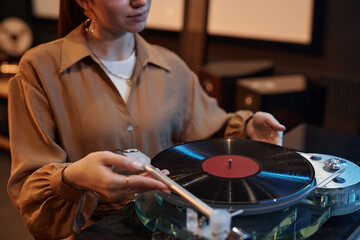 Closeup of young woman playing vinyl records at home in cozy setting, copy space