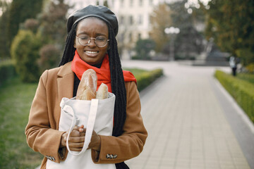 Young black woman in a coat standing outside holding a bag with a bread