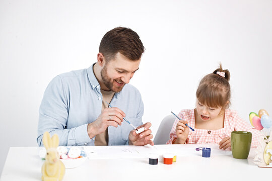 Girl with Down syndrome and her father painting Easter colored eggs